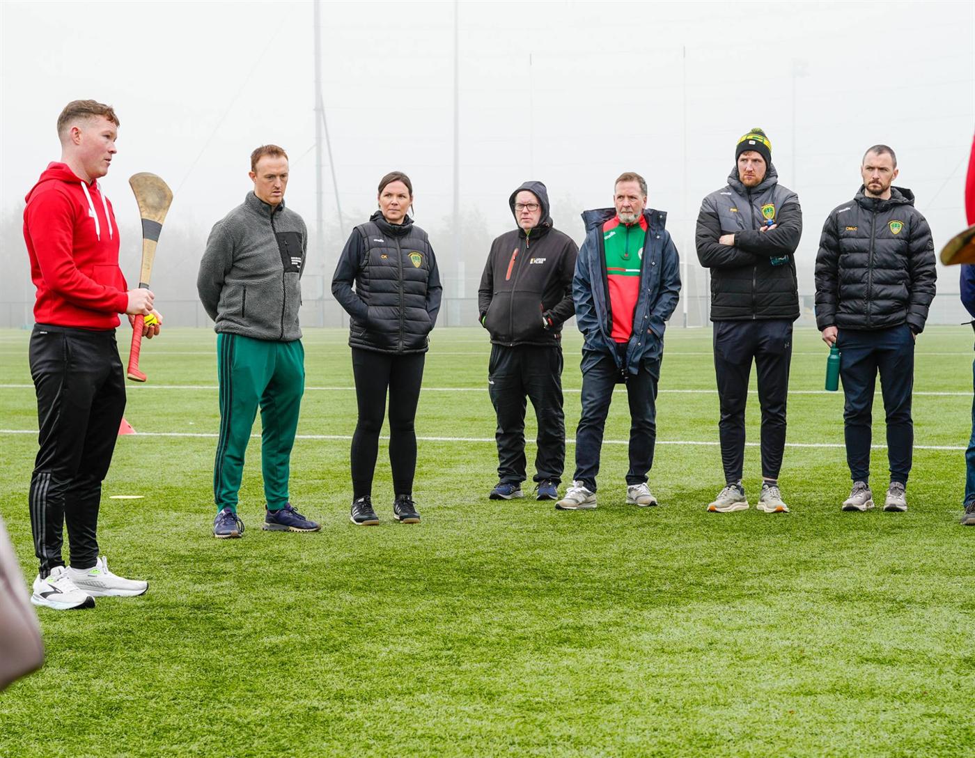 Shane talking to a group of coaches on the pitch, hurl in hand